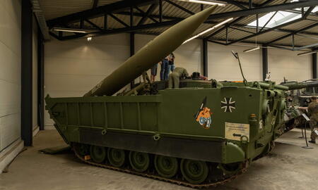 Ein grüner Militärpanzer mit Rakete wird in einem Museum ausgestellt, während Besucher ihn betrachten.
