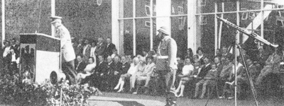 Bei einer feierlichen Zeremonie spricht ein Mann in Uniform am Podium vor einem Publikum, während ein Fernrohr aufgestellt ist.
