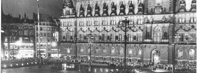 Eine große Menschenmenge versammelt sich abends vor dem hell erleuchteten Rathaus für eine feierliche Zeremonie.