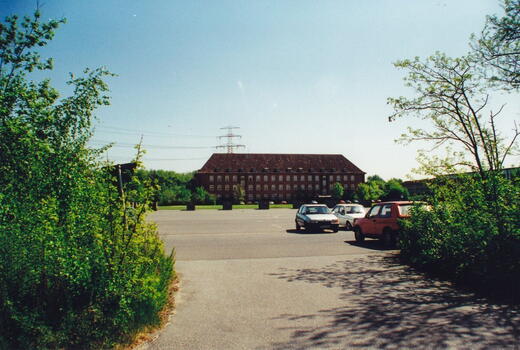 Mehrere Autos stehen 1994 auf dem Parkplatz der Bismarck-Kaserne, umgeben von grünen Bäumen und einem klaren Himmel.