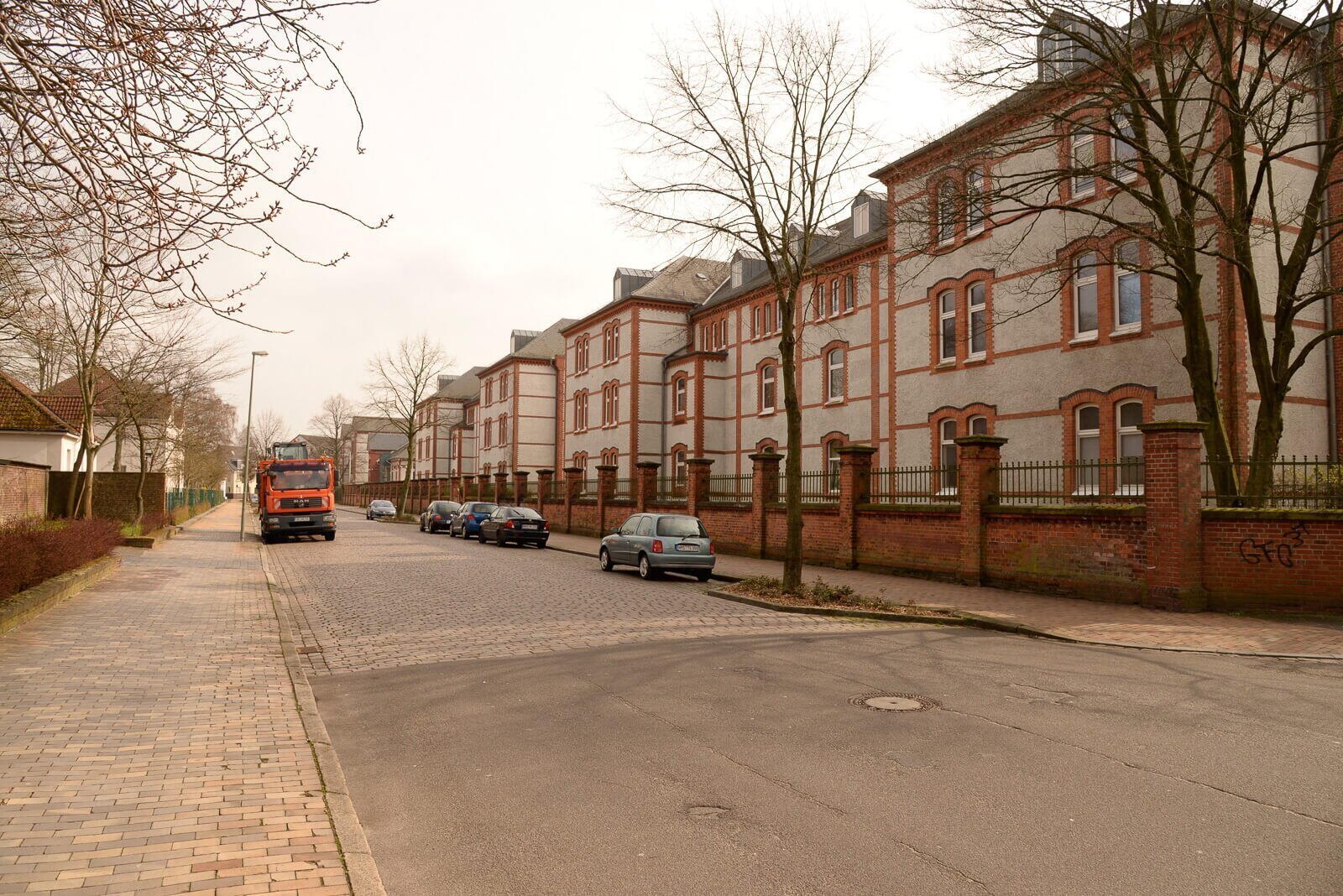 Eine ruhige Straße mit geparkten Autos und einem vorbeifahrenden Lastwagen vor einer Reihe historischer Gebäude.