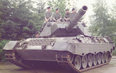 Soldaten in Uniform sitzen auf einem großen Panzer, umgeben von dichten Bäumen, im Freien.