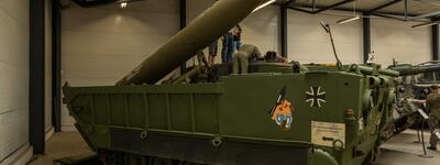 Ein grüner Militärpanzer mit Rakete wird in einem Museum ausgestellt, während Besucher ihn betrachten.