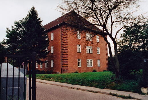 Ein rotes Backsteingebäude der Bismarck-Kaserne steht umgeben von Bäumen an einer gepflasterten Straße im Jahr 1996.