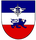 Ein Wappen zeigt einen blauen Löwen auf rotem Grund mit einem blauen und weißen Streifen darüber, gekrönt von einem Symbol.