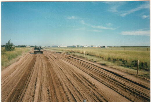 Ein Panzer fährt auf einer breiten, unbefestigten Straße durch eine offene Wiesenlandschaft unter klarem blauem Himmel.