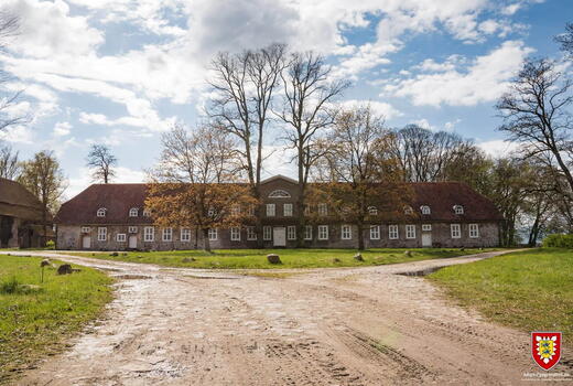 Ein großes, historisches Gebäude mit roten Dachziegeln steht vor einem bewölkten Himmel in Lanken.