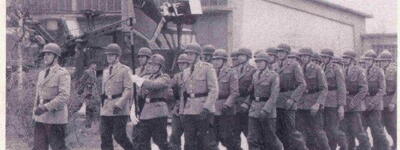 Soldaten marschieren in Formation, um feierlich die Truppenfahne am 29. April 1965 vor einem Gebäude einzuholen.