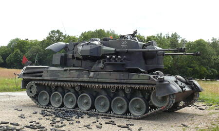 Ein gepanzerter Flakpanzer steht auf einem Übungsgelände, umgeben von verbrauchten Patronenhülsen.