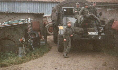 Soldaten in Uniformen posieren auf einem Militärfahrzeug vor einer Scheune während einer Übung 1988.