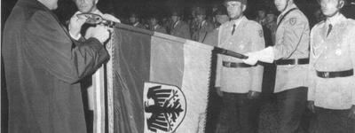 Ein Mann überreicht einem Soldaten des Panzerbataillons 184 ein Fahnenband, während mehrere Soldaten salutieren.