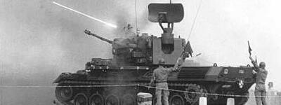 Ein Flakpanzer Gepard feuert auf dem Truppenübungsplatz Todendorf, während zwei Soldaten daneben stehen.