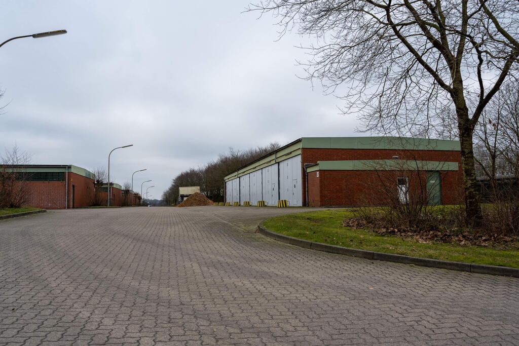 Ein leerer Industriehof mit roten Backsteingebäuden und kahlen Bäumen unter einem bewölkten Himmel.