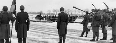 Soldaten stehen in der verschneiten Landschaft in Formation, während ein Militärfahrzeug vorbeifährt.