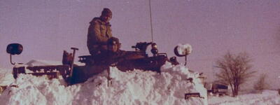 Ein Panzer pflügt durch tiefen Schnee, während zwei Soldaten oben darauf sitzen.