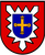 Ein Wappen zeigt ein gelbes Kreuz mit Blumen auf blauem Schild, umgeben von einem roten Rand mit weißer Zackenform.
