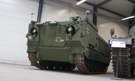 Ein großer, olivgrüner Militärpanzer steht in einer Ausstellungshalle, umgeben von weiteren historischen Fahrzeugen.