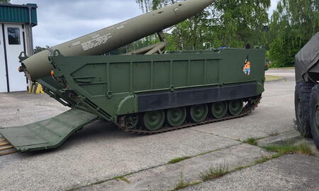 Ein grünes Militärfahrzeug mit einer großen Rakete ist in einem offenen Bereich neben einem Gebäude geparkt.