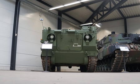 Zwei Militärfahrzeuge stehen in einer Halle nebeneinander, eines davon ist ein grüner Panzer mit der Nummer 16.