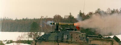 Ein Panzer feuert eine Rakete in einer verschneiten Landschaft mit Wäldern im Hintergrund ab.