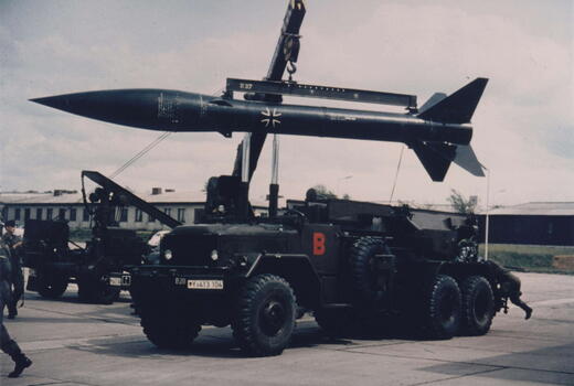 Ein Militärfahrzeug transportiert eine Rakete mit einem Kran auf einem Flugplatz.