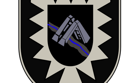 Ein Wappen zeigt ein stilisiertes Brückensymbol mit einem blauen Fluss, umgeben von einem gezackten Rand.