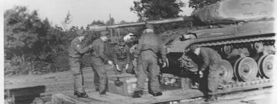 Soldaten verladen Ausrüstung neben einem Panzer auf einem Güterzug, um eine militärische Operation vorzubereiten.