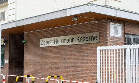 Das Schild der Oberst-Herrmann-Kaserne ist an einer Backsteinwand neben einem weißen Tor befestigt.