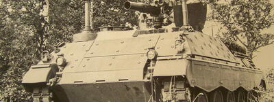 Ein gepanzerter Militärpanzer steht inmitten einer bewaldeten Landschaft, umgeben von dichtem Grün.