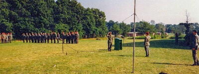 Soldaten stehen in Formation auf einer Wiese in Bergen-Hohne, während ein Offizier salutiert und eine Rede hält.