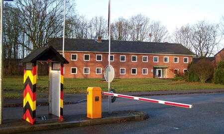Ein rotes Stabsgebäude mit Schranke und Wachhäuschen im Vordergrund in der Lettow-Vorbeck-Kaserne.