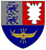 Das Wappen zeigt zwei blaue Löwen, ein weißes Zickzack-Muster und ein geflügeltes Zahnrad auf dunkelblauem Hintergrund.