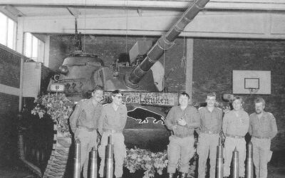 Soldaten posieren vor dem ersten M48-Panzer mit 105-mm-Kanone in einer Halle, umgeben von Granathülsen und Dekorationen.