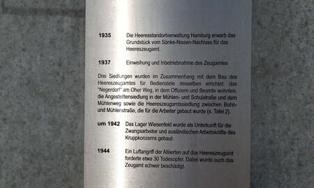 Eine Metalltafel an einer grauen Wand beschreibt historische Ereignisse des Heereszeugamts von 1935 bis 1944.