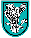 Ein stilisiertes Wappen zeigt eine Eule, die auf einem Ast sitzt, umgeben von einem türkisfarbenen Hintergrund.