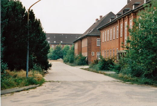 Eine ruhige Straße führt durch die Bismarck-Kaserne, flankiert von roten Backsteingebäuden und üppigem Grün.