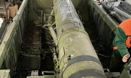 Ein großer, altertümlicher Raketenwerfer liegt in einer Werkstatt mit Regalen im Hintergrund.