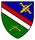 Ein Wappen zeigt gekreuzte Werkzeuge und Gewehre auf blau-grünem Grund mit roten und weißen Streifen.