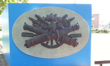 Ein kunstvolles Denkmal mit historischen Kanonen und Waffen ist auf einer blauen Tafel im Freien ausgestellt.
