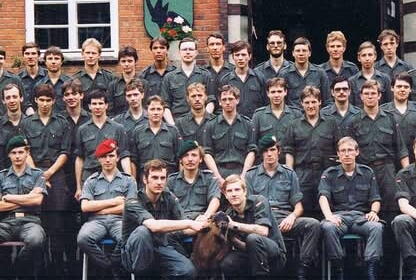 Eine Gruppe von Soldaten in Uniform posiert vor einem Backsteingebäude für ein Gruppenfoto.
