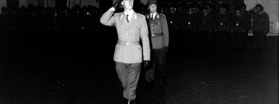 Ein Offizier in Uniform salutiert, während er mit Soldaten in einer Halle marschiert.