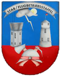 Ein Wappen zeigt einen Kontrollturm, einen Leuchtturm und einen Helm mit gekreuzten Schwertern unter einer Wolke.
