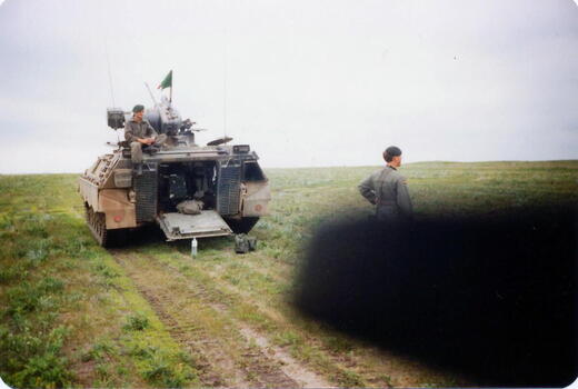 Ein Soldat sitzt auf einem Panzer, während ein anderer auf einer Wiese bei Deilingshofen steht und in die Ferne blickt.