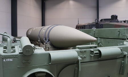 Ein grünes Militärfahrzeug im Innenraum transportiert eine große, spitz zulaufende Rakete.
