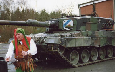 Ein Mann in mittelalterlicher Kleidung steht neben einem Leopard-2-Panzer, der mit einem Wappen von Till von Mölln verziert ist.