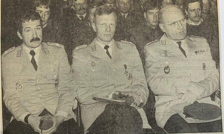 Drei Männer in Militäruniformen sitzen nebeneinander bei einer Veranstaltung in Ladelund zwischen 1972 und 1987.