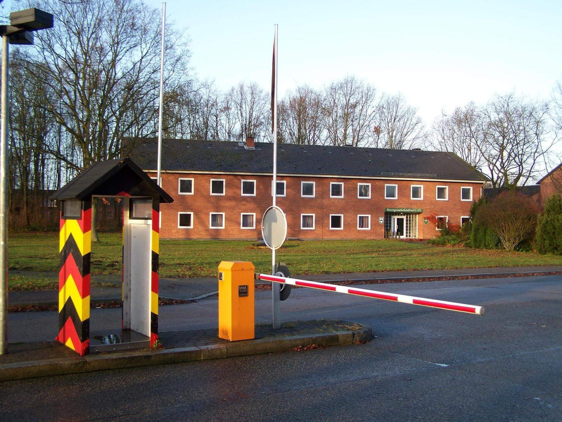 Ein rotes Stabsgebäude mit Schranke und Wachhäuschen im Vordergrund in der Lettow-Vorbeck-Kaserne.