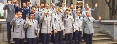 Eine Gruppe von Männern in Uniformen steht auf einer Treppe und winkt fröhlich in die Kamera.