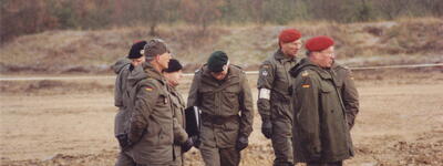 Mehrere uniformierte Soldaten stehen im Freien und besprechen die Einweisung für ein Marschschießen auf einem Übungsplatz.