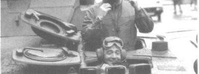 Zwei Männer mit Kopfhörern schauen aus einem geöffneten Panzer, einer sitzt drinnen, der andere steht oben.